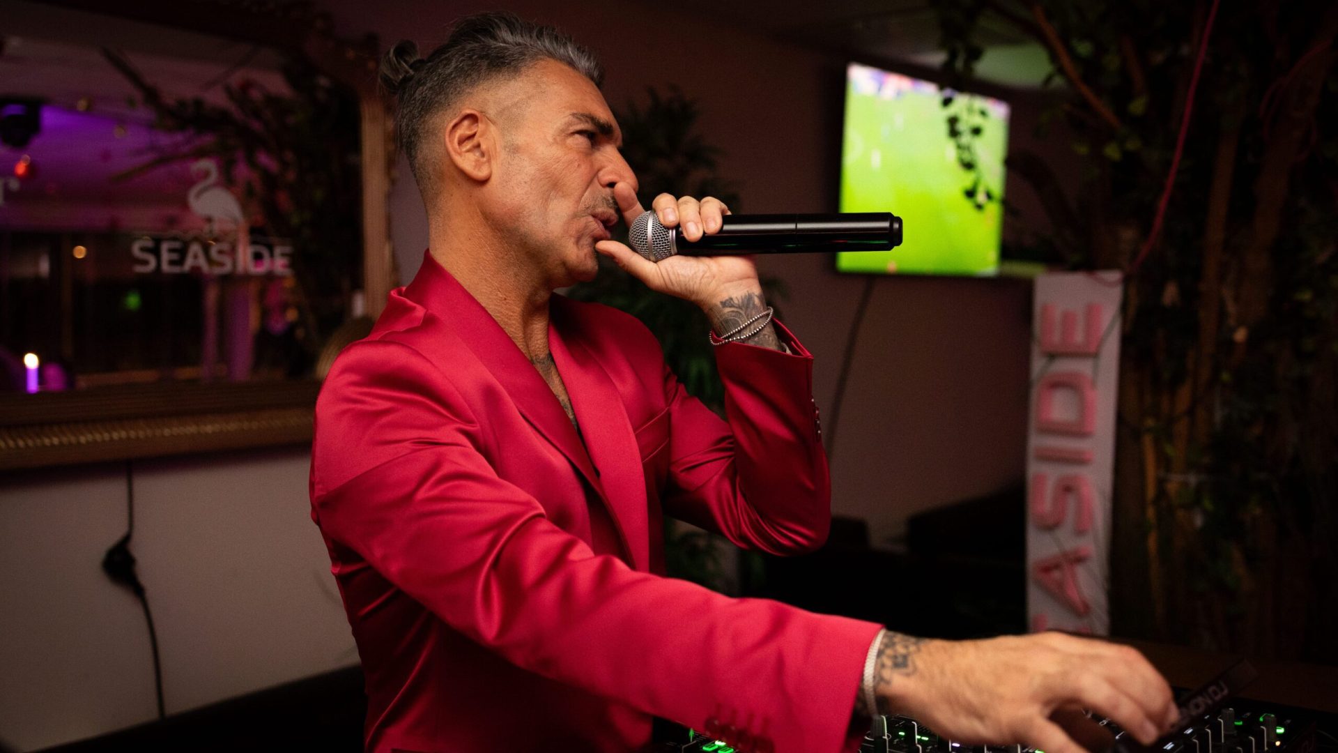 Ritratto di profilo di un vocalist in giacca fucsia accesa mentre parla al microfono.